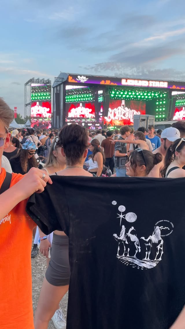 Black Confused Minds desert tee held up in the crowd at a festival stage