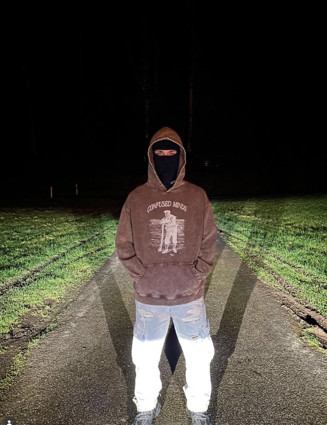 Model in a washed brown Confused Minds hoodie standing on a road at night
